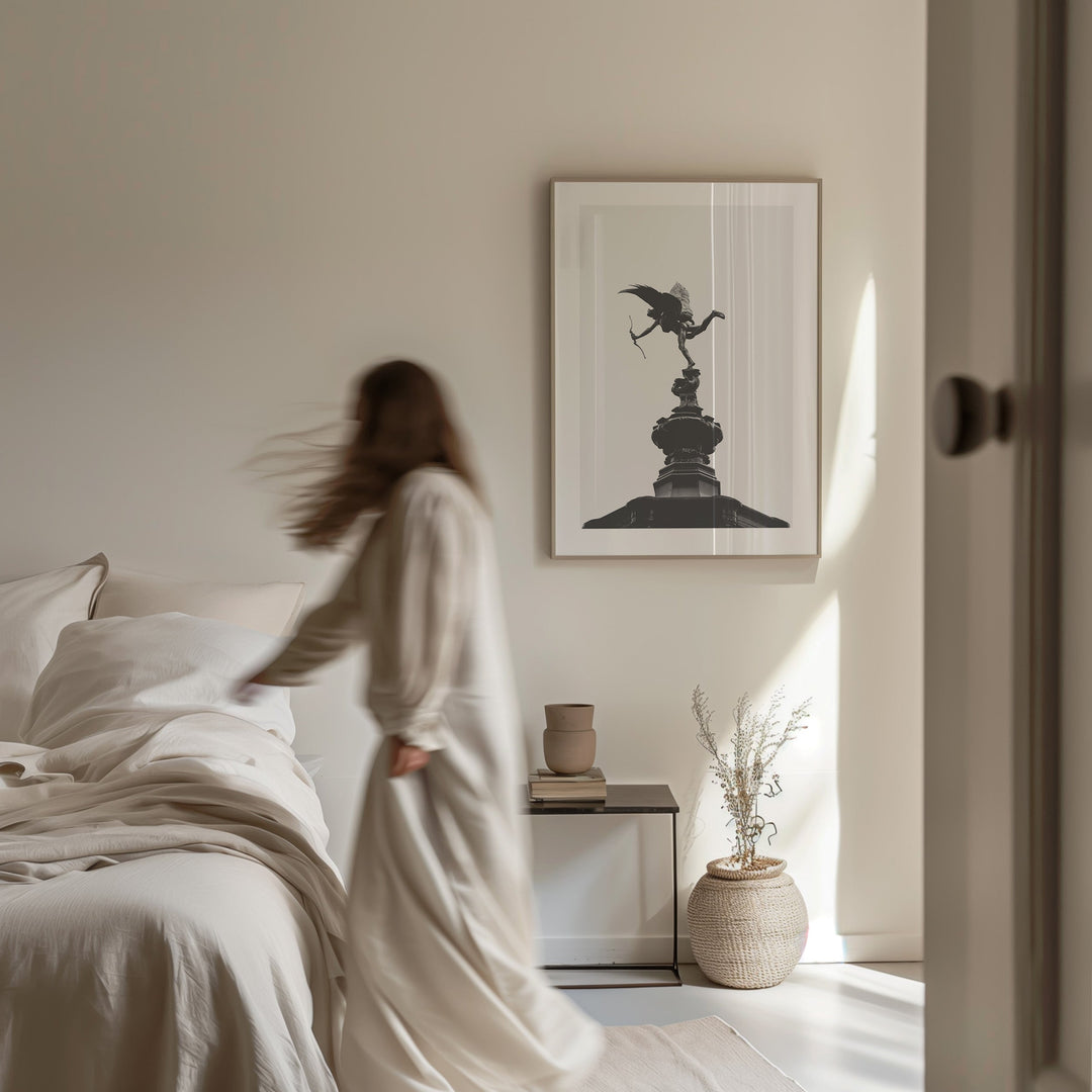 Framed black and white art print of the Anteros water fountain, in a thin natural wood frame by a modern bedside scene.